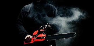Person holding a red chainsaw in a dark, smoky setting