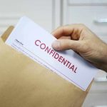 Hand placing confidential document into a brown envelope