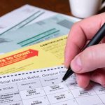 Hand filling out a mail-in ballot with a pen