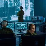 Military analysts monitor data on multiple screens in a command center