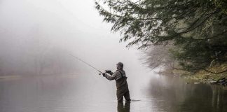 Angler wading in a foggy river casting a fishing rod