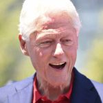 Bill Clinton smiling outdoors in a blue blazer and red shirt