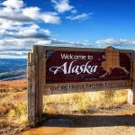Democrats Accused of Planting a DECOY Candidate wooden welcome sign with Alaska map by open landscape