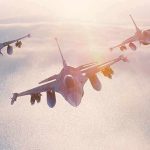 Three fighter jets flying in formation above clouds at sunrise
