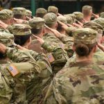 Soldiers in camouflage uniforms salute in formation
